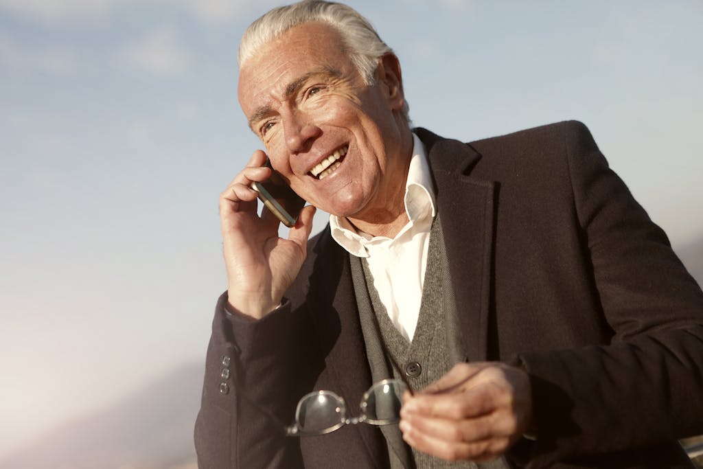 Senior man in a suit, smiling while talking on a smartphone, enjoying leisure outdoors.