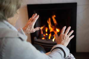 Senior Woman Warming Hands By Fire At Home